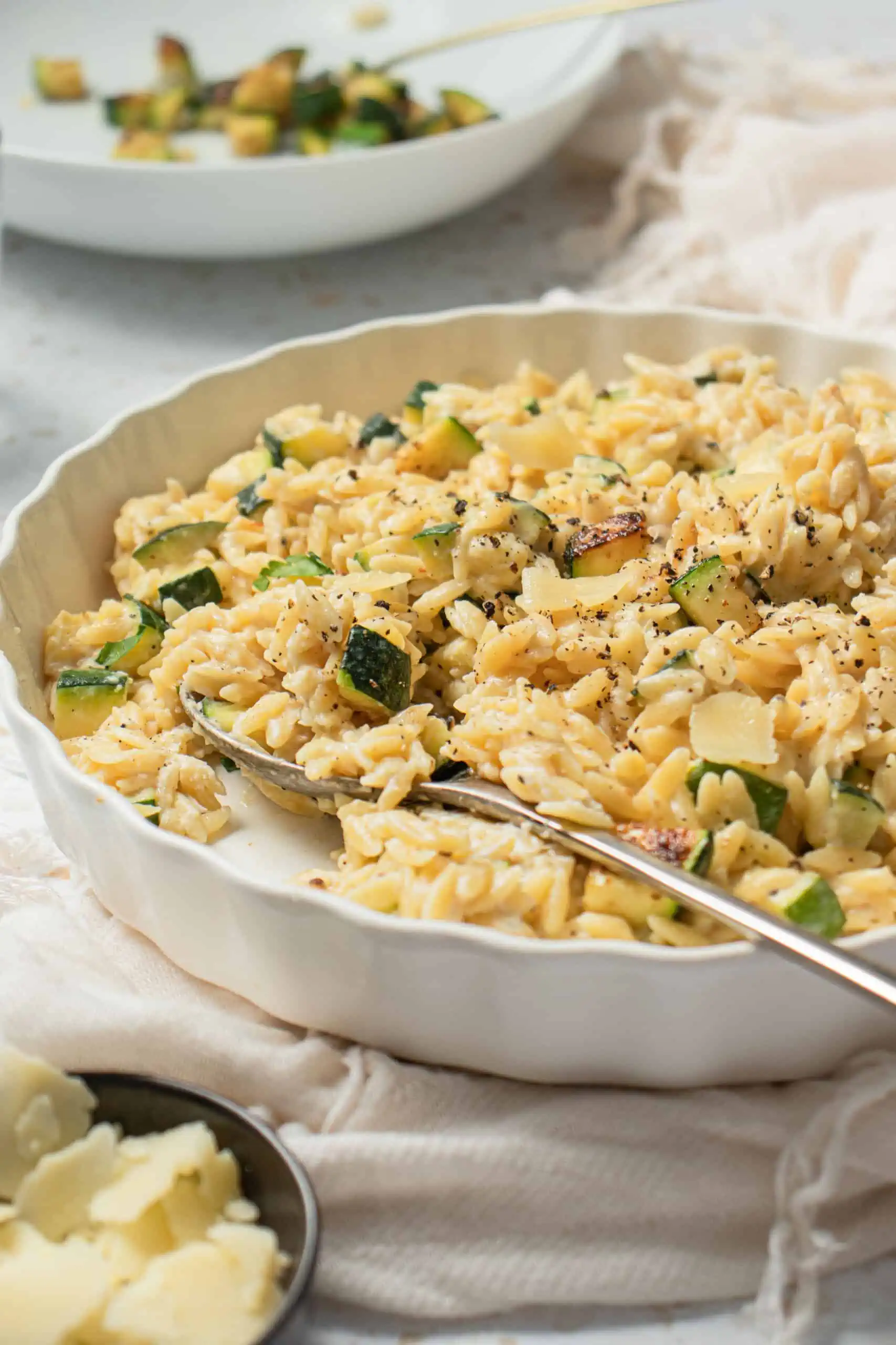 a vibrant and decadent dish that captures the essence of freshness and wholesome ingredients. The orzo, a small rice-shaped pasta, is cooked to perfection, exhibiting a tender yet slightly firm texture. The zucchini, cut into bite-sized pieces, is scattered generously throughout the dish, adding a pop of green color and contributing a crisp and succulent element.