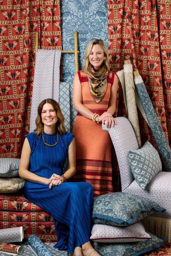 Two women sitting and smiling in front of textiles.